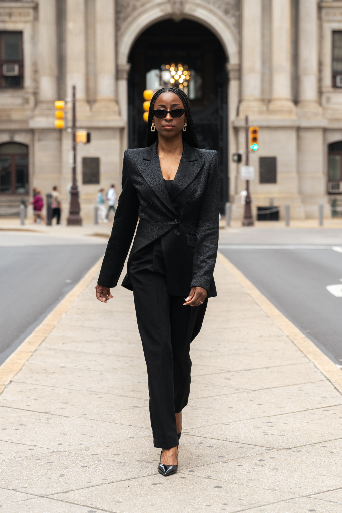 Woman in a black suit walking on a city street.