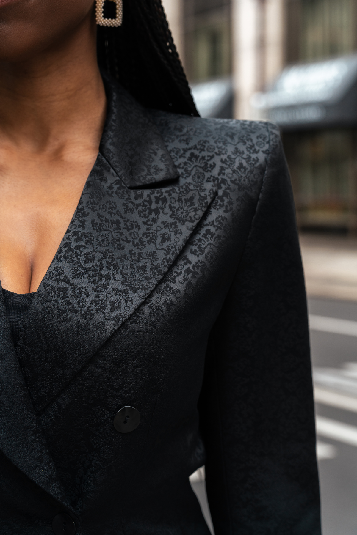 Close-up of a person wearing a black patterned blazer outdoors.