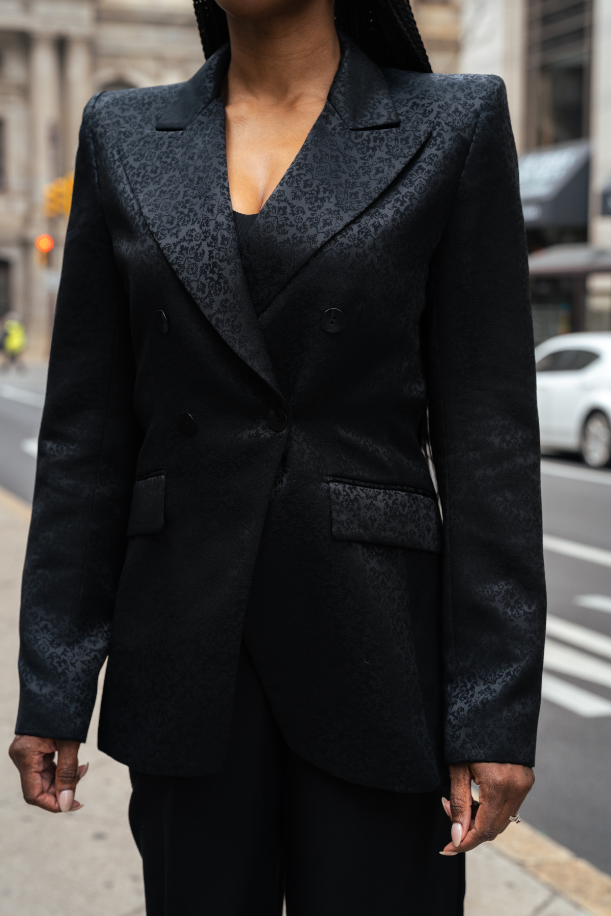Person wearing a dark textured suit jacket on a city street.