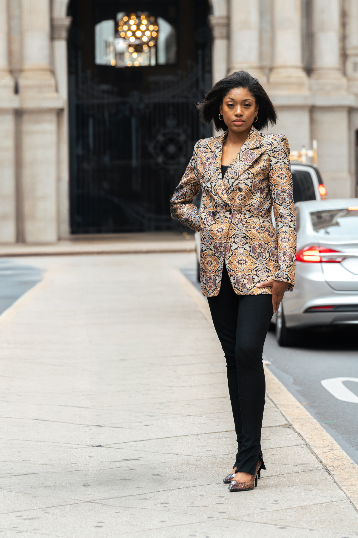 Woman in a patterned blazer walking on a city street.