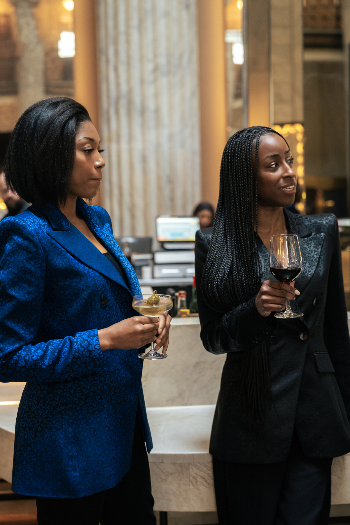 Two women in formal attire holding drinks in an indoor setting