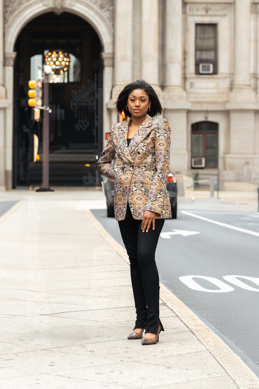 Woman in a patterned blazer standing on a city street with a building in the background