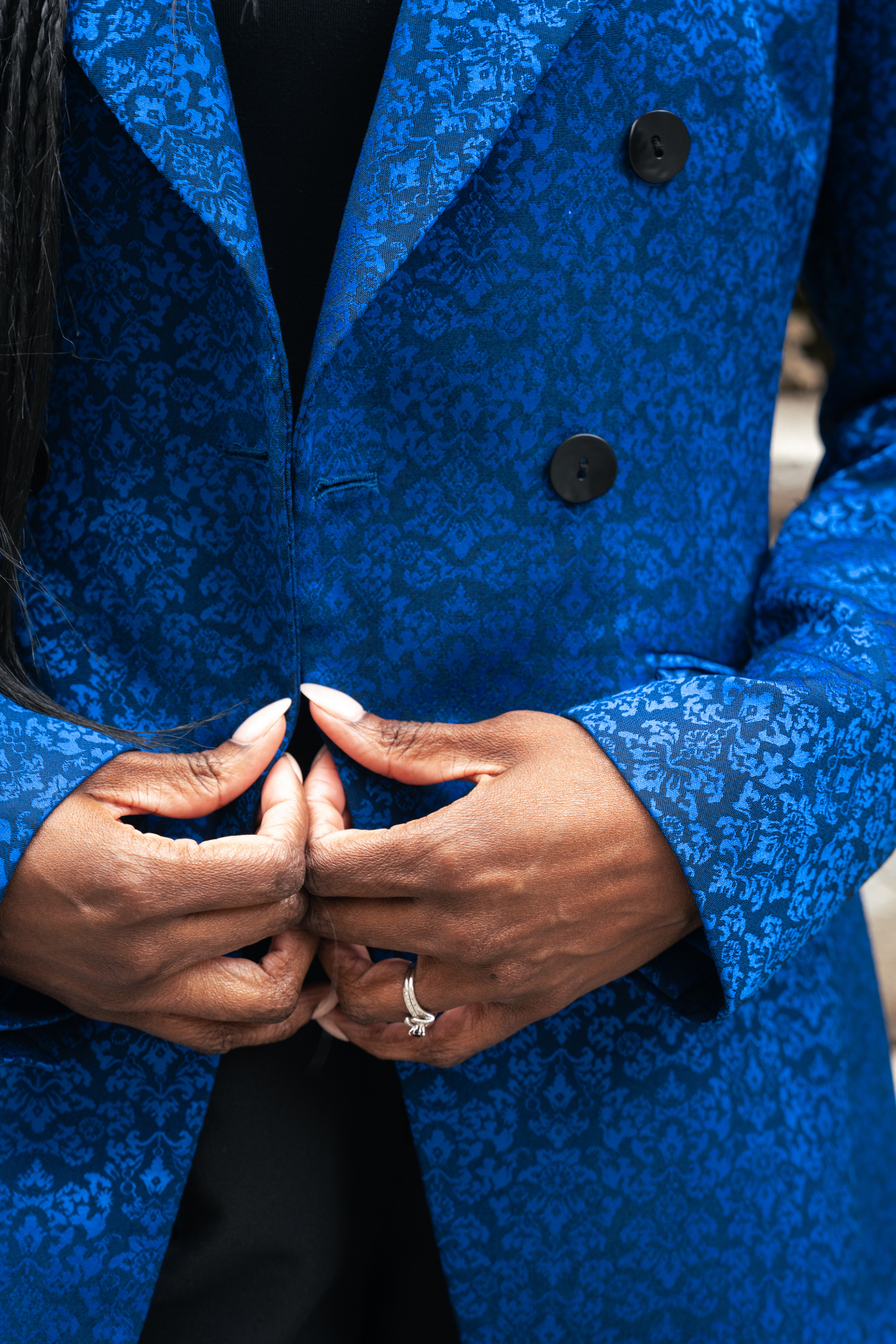 Close-up of a person wearing a blue textured coat with hands clasped together.