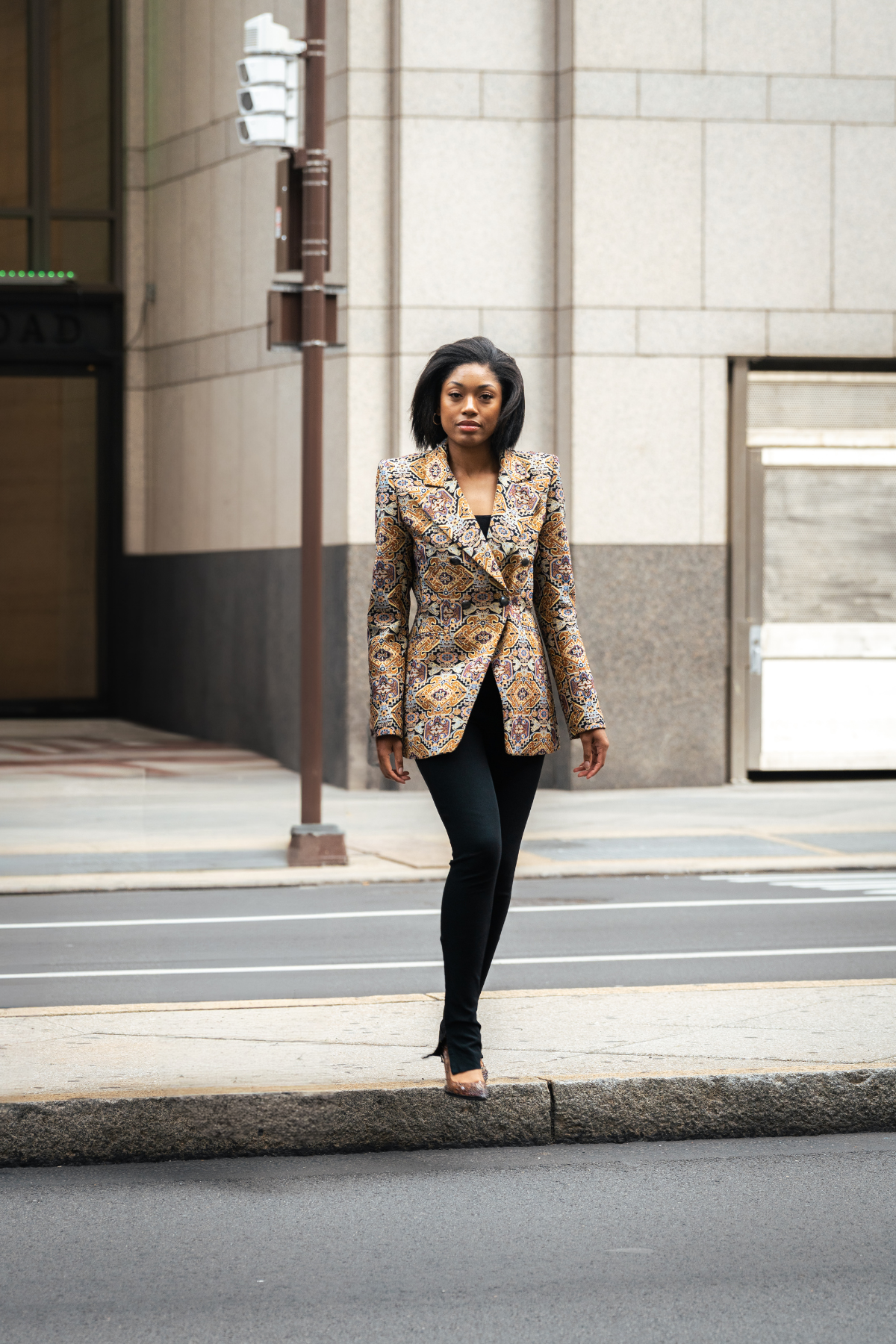 Woman in a patterned blazer walking on a city street.