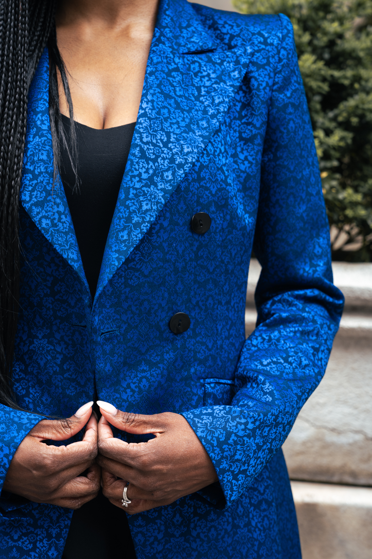 Blue floral-patterned coat with black buttons worn by a person, blurred background