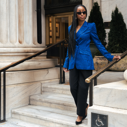 Woman in a blue blazer and black pants standing on marble steps outside a building.