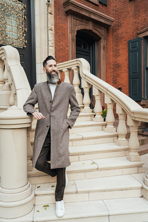 Man in a brown coat standing on stone steps in front of a brick building