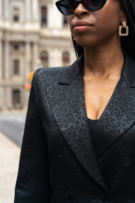 Person wearing a black patterned blazer with a blurred city street background