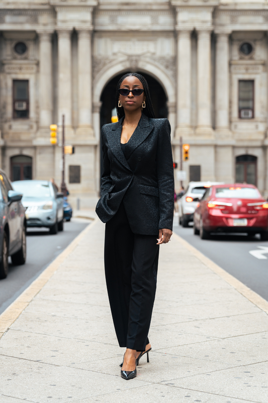 Woman in a black suit standing on a city street with cars and traffic lights in the background.
