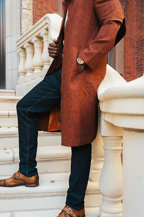 Person wearing a brown coat and dark jeans sitting on stone steps.