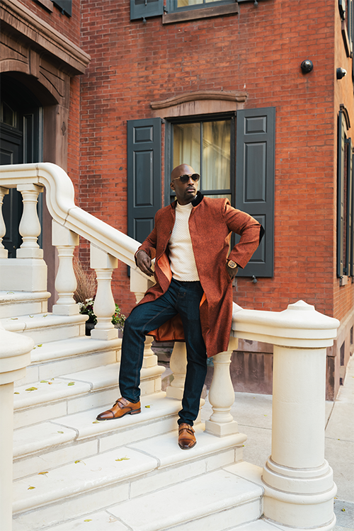 Man in a long coat standing on stone steps in front of a brick building