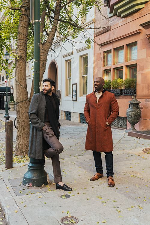 Two men standing on a city street, one in a gray coat and the other in a brown coat.