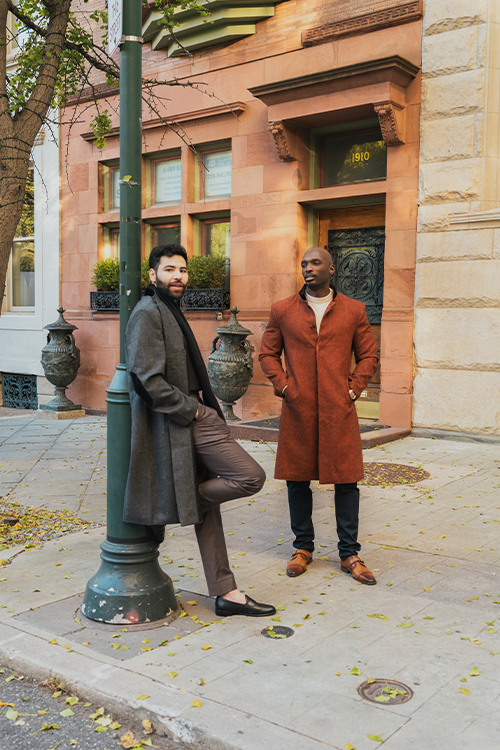 Two men standing on a sidewalk in front of a building with decorative elements.