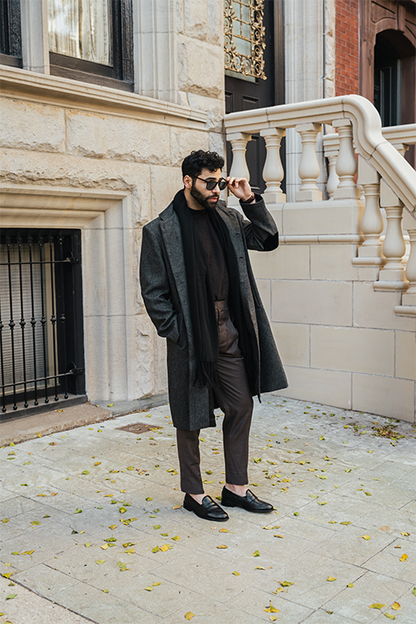 Man in a dark coat and suit standing on a sidewalk with a building in the background