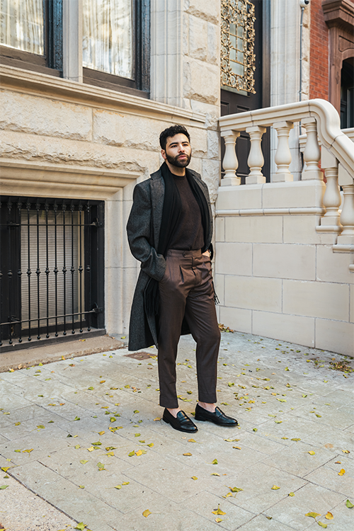 Man in a stylish outfit standing on a stone pavement with classical architecture in the background