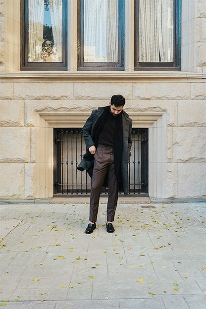 Man in a coat and suit standing in front of a stone building with large windows.