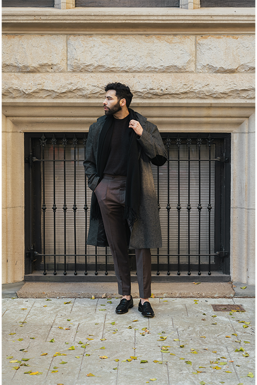 Man in a long coat standing in front of a stone building with metal bars.