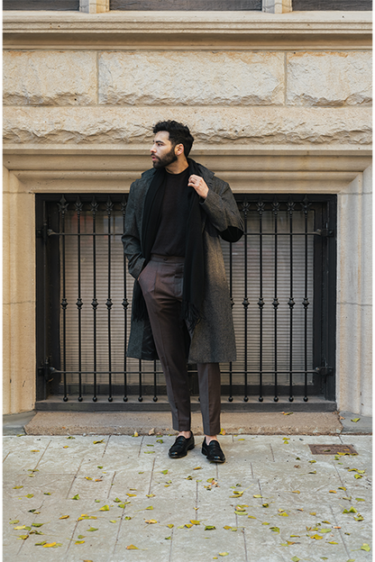 Man in a long coat standing in front of a stone building with metal bars.