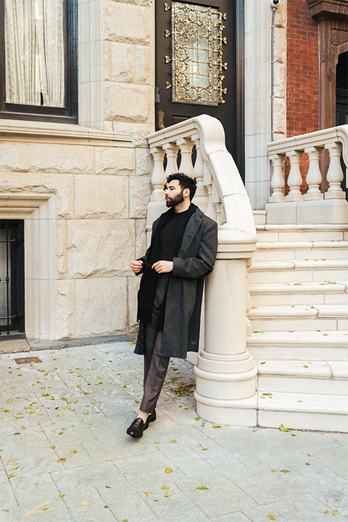 Man in a long coat standing on a stone staircase in an urban setting