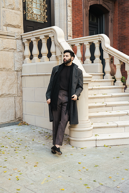 Man in a gray coat standing on stone steps in an urban setting