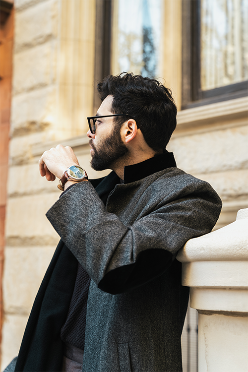 Man in a gray coat standing against a building wall