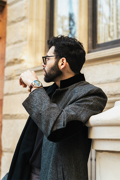 Man in a gray coat standing against a building wall