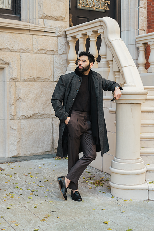 Man in a long coat standing on a stone staircase in an urban setting