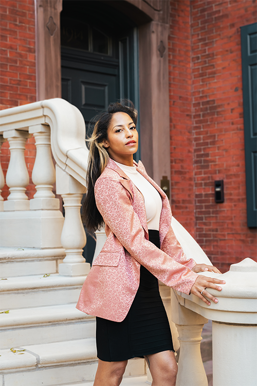 Woman in a pink blazer standing on steps with a brick building in the background