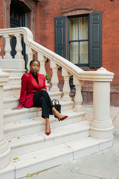 Woman in a red jacket sitting on stone steps in front of a brick building.