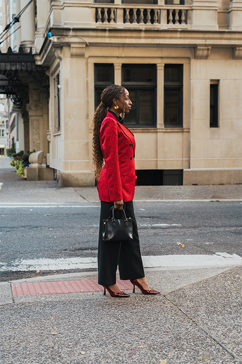 Woman in a red coat standing on a city street corner.