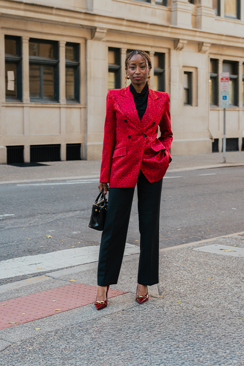 Woman in a red blazer and black pants standing on a city street.