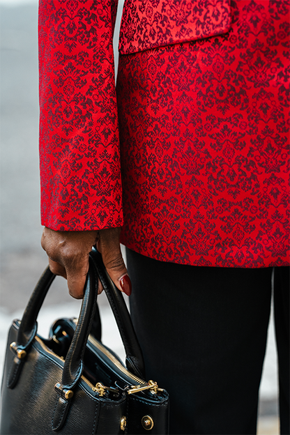 Person wearing a red patterned coat holding a black handbag.