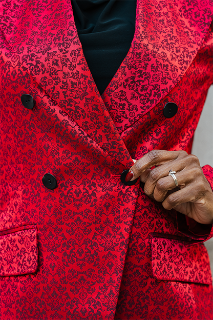 Red patterned coat with a hand adjusting a button, wearing a ring.