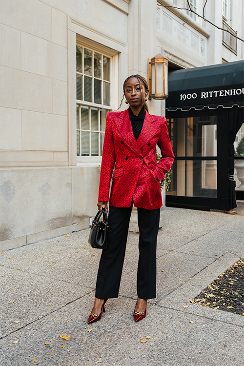 Woman in a red blazer and black pants standing on a city street.